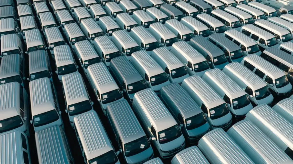 Rangée d'utilitaires et de voitures de société alignés sur un parking d'entreprise, vue large